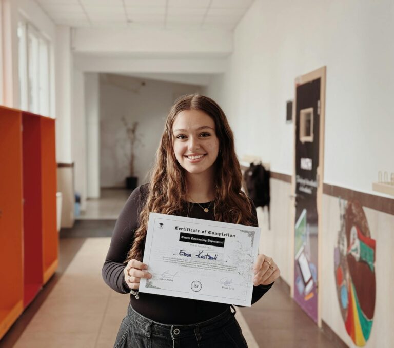 young woman holding certificate in school hallway