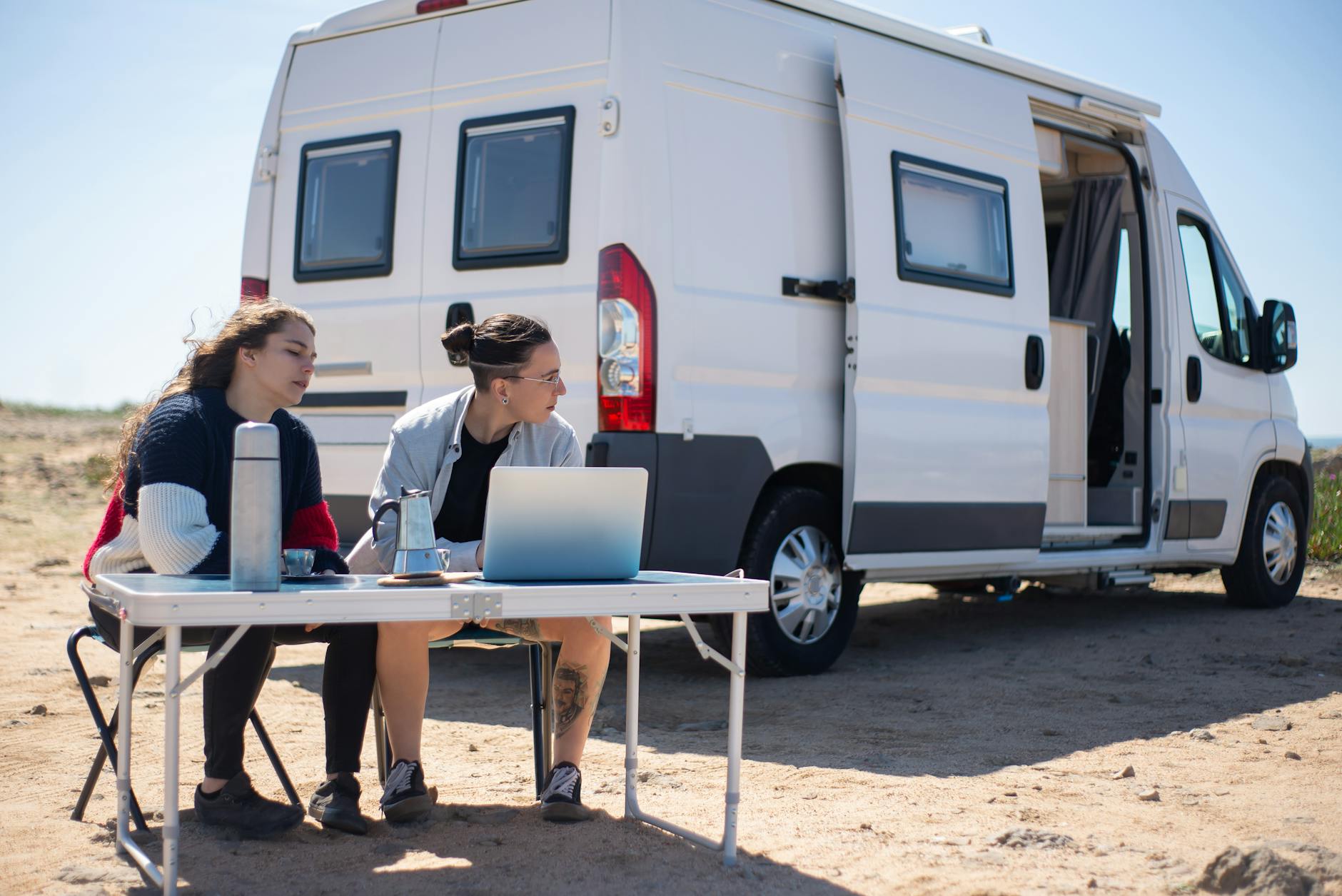 a man and woman sitting at a table with laptop near a trailer